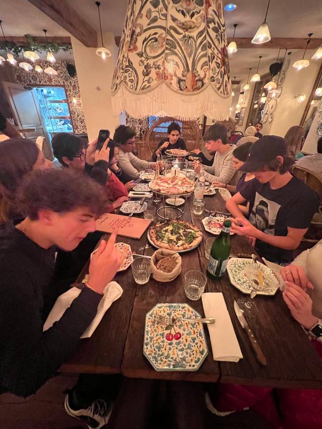 Students have dinner around a long wooden table in a restaurant with hanging lamps.