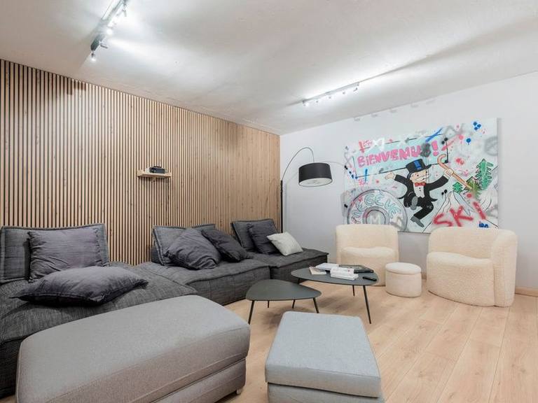 A large living room with gray sofas, white armchairs, light wood floors, and a colorful painting on the wall.