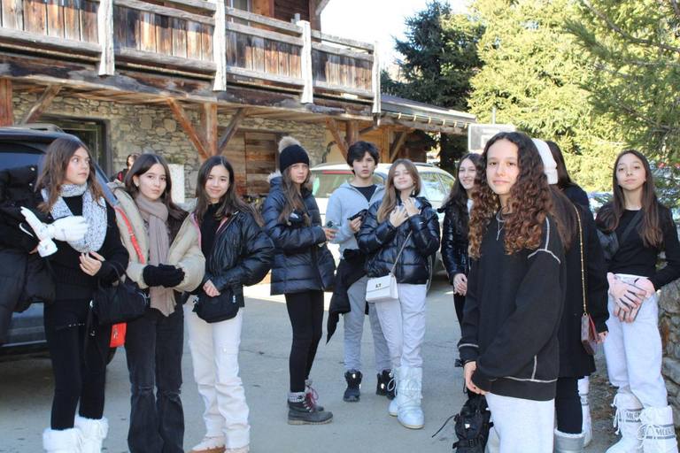 A group of students in winter jackets poses in front of a wooden chalet.