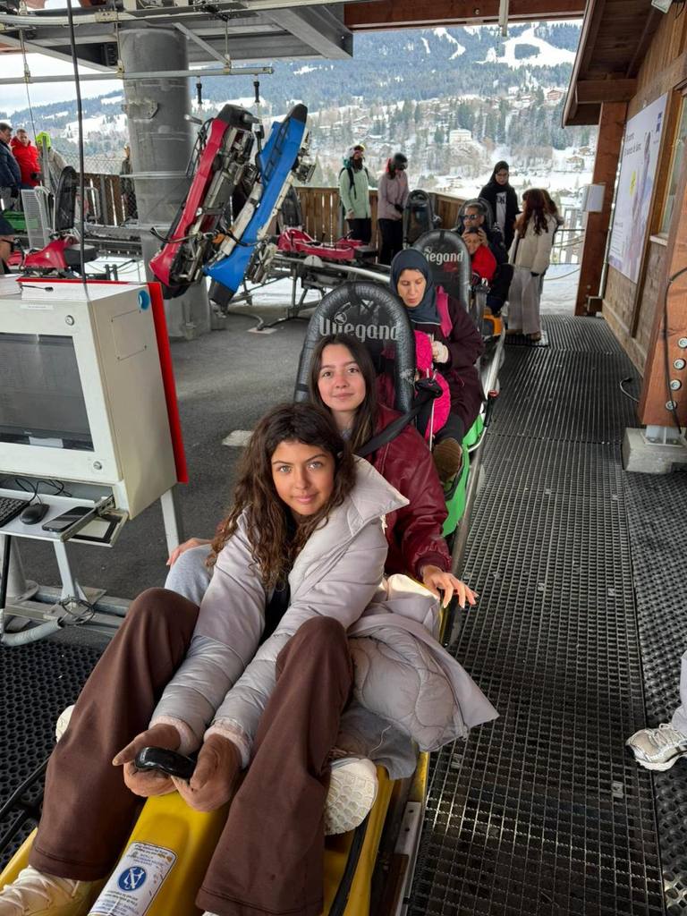Students sit in the starting cars of a mountain coaster on rails, with a snowy valley behind them.