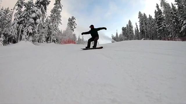 A skier carves down a freshly groomed run between snow-covered pines, under a blue sky with high clouds.