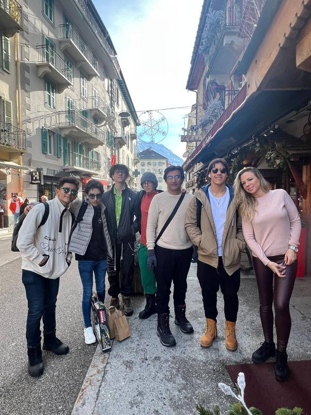 Seven students and a chaperone pose in winter coats on a street in an alpine village.